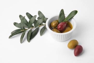 Photo of Bowl with different ripe olives and leaves on white background