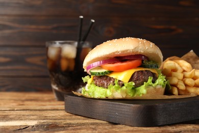 Delicious burger, soda drink and french fries served on wooden table, closeup. Space for text
