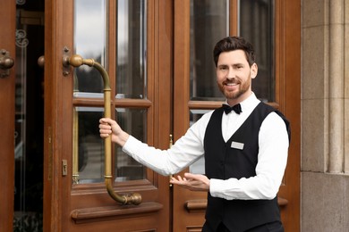 Photo of Butler in elegant suit opening wooden hotel door. Space for text