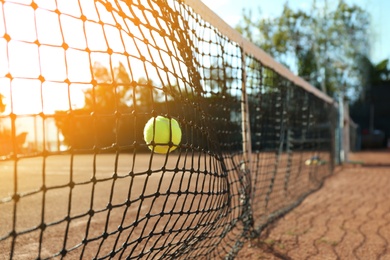 Photo of Bright yellow tennis ball hitting into net on court
