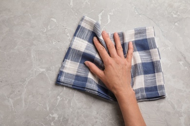 Photo of Woman wiping marble table with kitchen towel, top view. Space for text