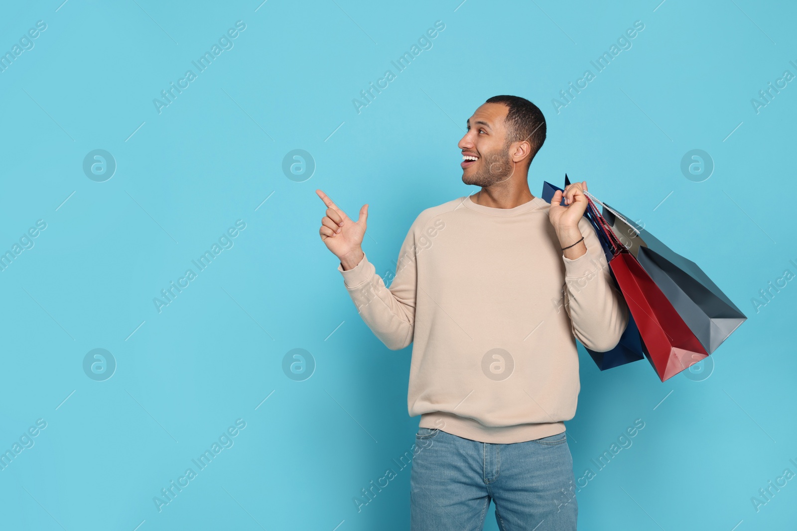 Photo of Happy African American man with shopping bags on light blue background. Space for text