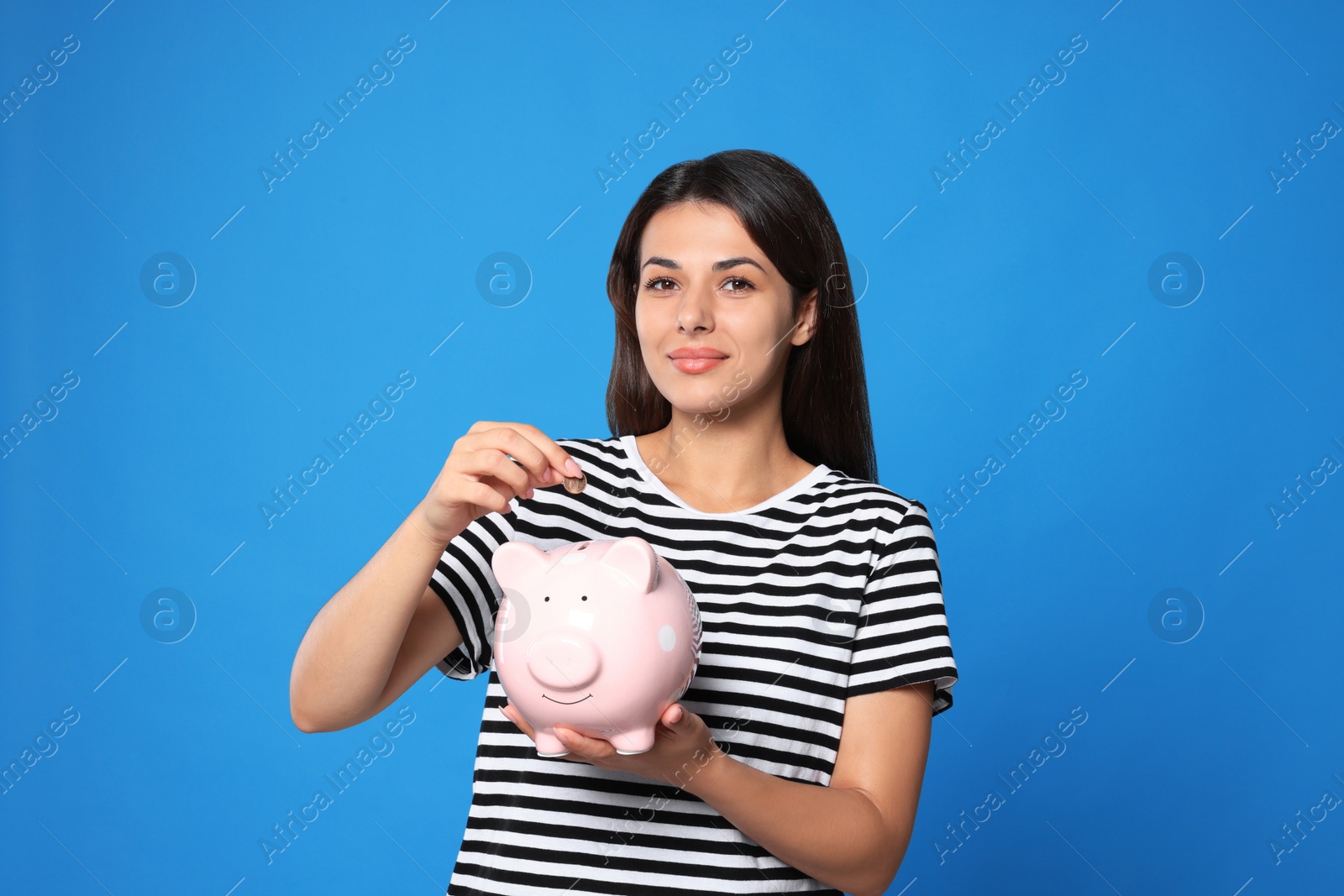 Photo of Young woman putting coin into piggy bank on light blue background