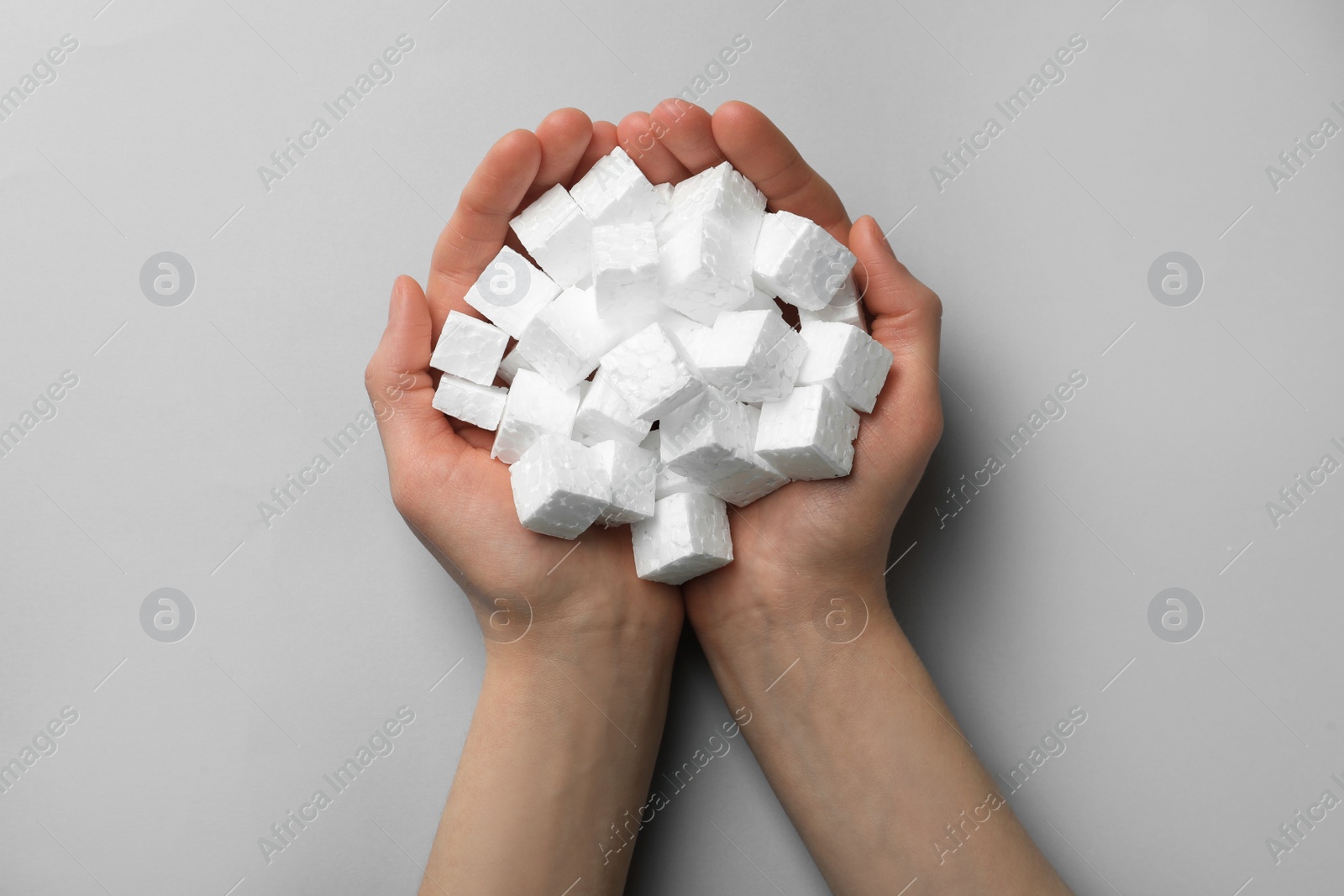 Photo of Woman with handful of styrofoam cubes on light grey background, top view