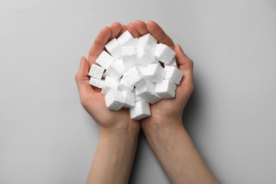 Woman with handful of styrofoam cubes on light grey background, top view