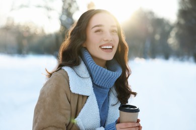 Photo of Portrait of smiling woman with paper cup of coffee in snowy park