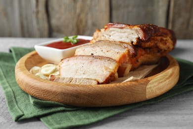 Photo of Pieces of baked pork belly served with sauce on grey wooden table, closeup