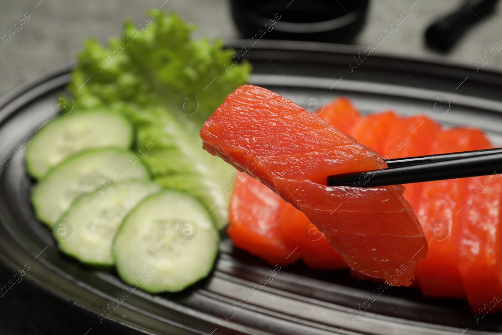 Photo of Taking tasty salmon slice with chopsticks from plate, closeup. Delicious sashimi dish