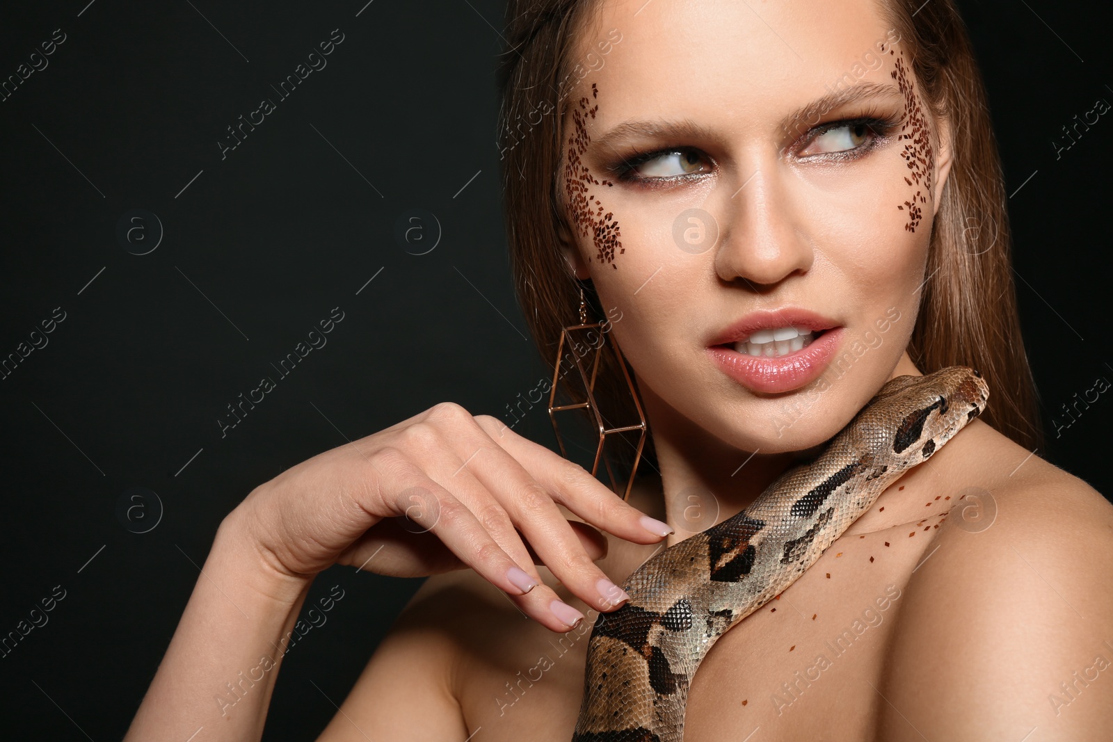 Photo of Beautiful woman with boa constrictor on black background, closeup