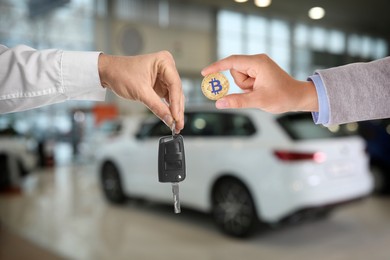 Image of Bitcoin exchange. Man using cryptocurrency to buy auto. Seller holding key and buyer with bitcoin in car dealership, closeup