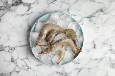 Photo of Raw shrimps with ice on marble table, top view