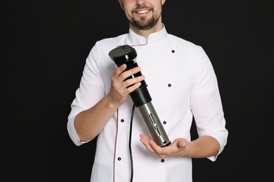 Smiling chef holding sous vide cooker on black background, closeup