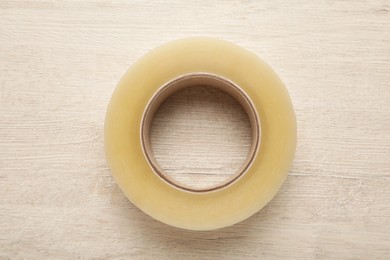 Photo of Roll of adhesive tape on wooden background, top view