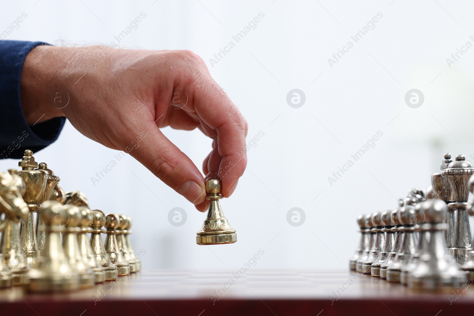 Photo of Man with game piece playing chess at checkerboard against white background, closeup