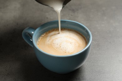 Photo of Pouring milk into cup of coffee on grey table, closeup