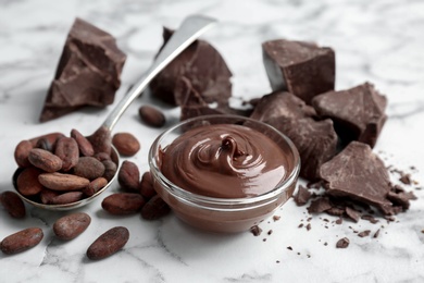 Bowl with tasty melted chocolate, chunks and cocoa beans on table