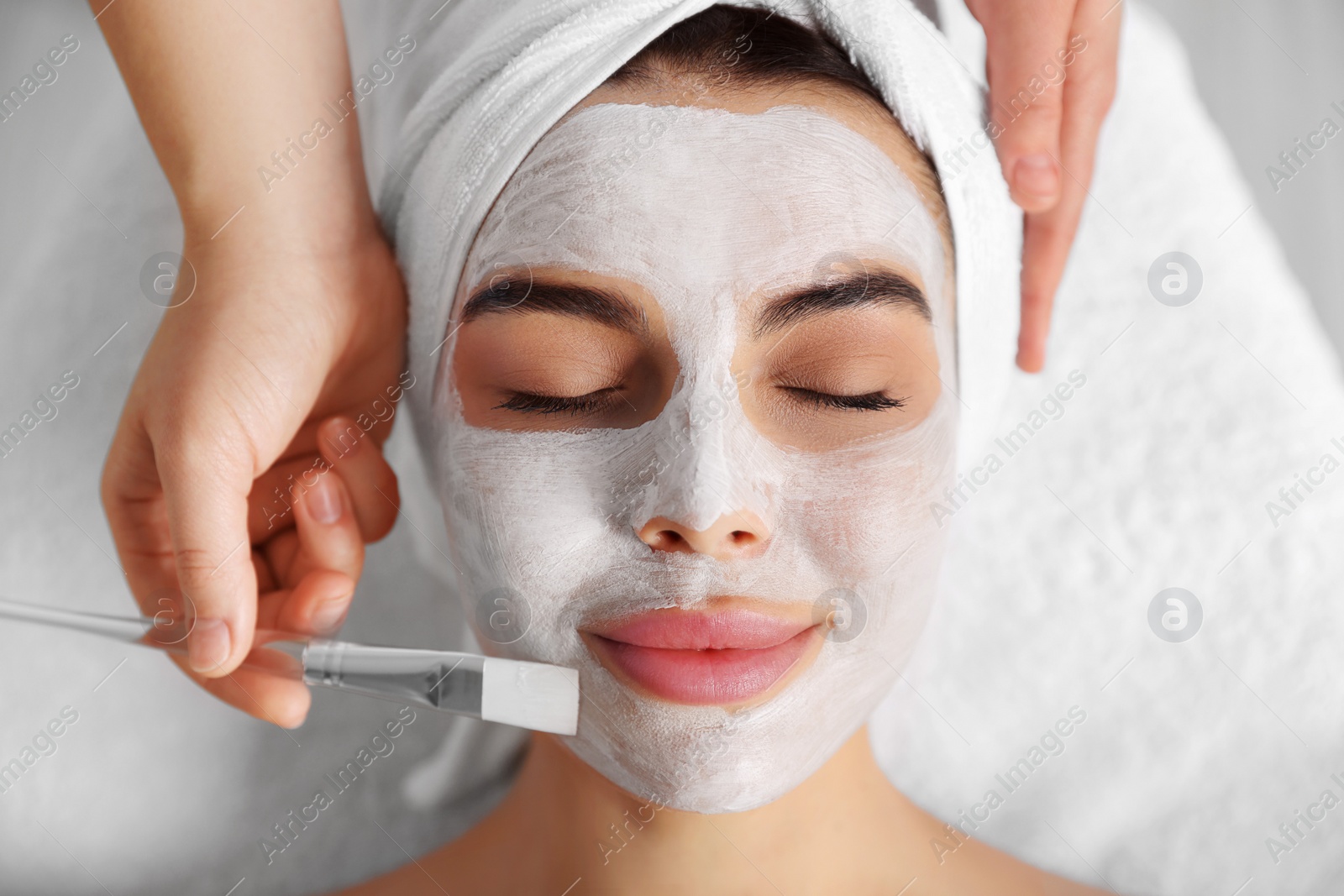 Photo of Cosmetologist applying mask on woman's face in spa salon, closeup. Top view