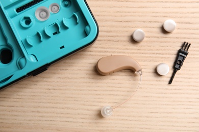 Photo of Hearing aid, case and accessories on wooden background, top view