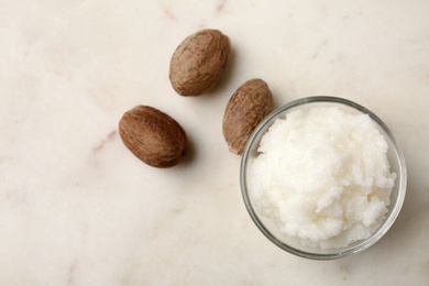 Photo of Shea butter in bowl and nuts on table, top view. Space for text