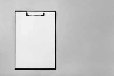 Photo of Black clipboard with sheet of blank paper on light grey background, top view. Space for text