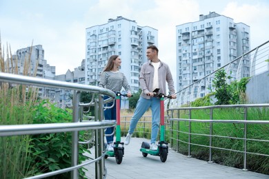 Photo of Happy couple riding modern electric kick scooters on city street