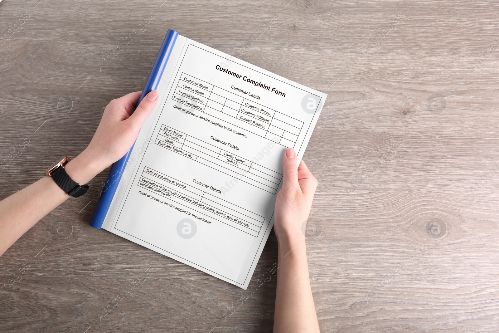 Image of Woman holding complaint form at wooden table, top view