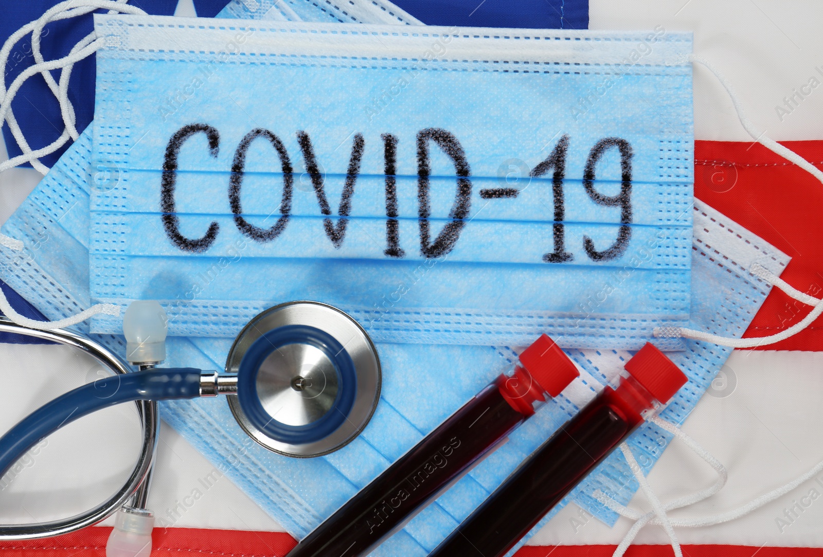 Photo of COVID-19 written on protective mask, test tubes with blood, stethoscope and American flag, flat lay. Coronavirus pandemic in USA