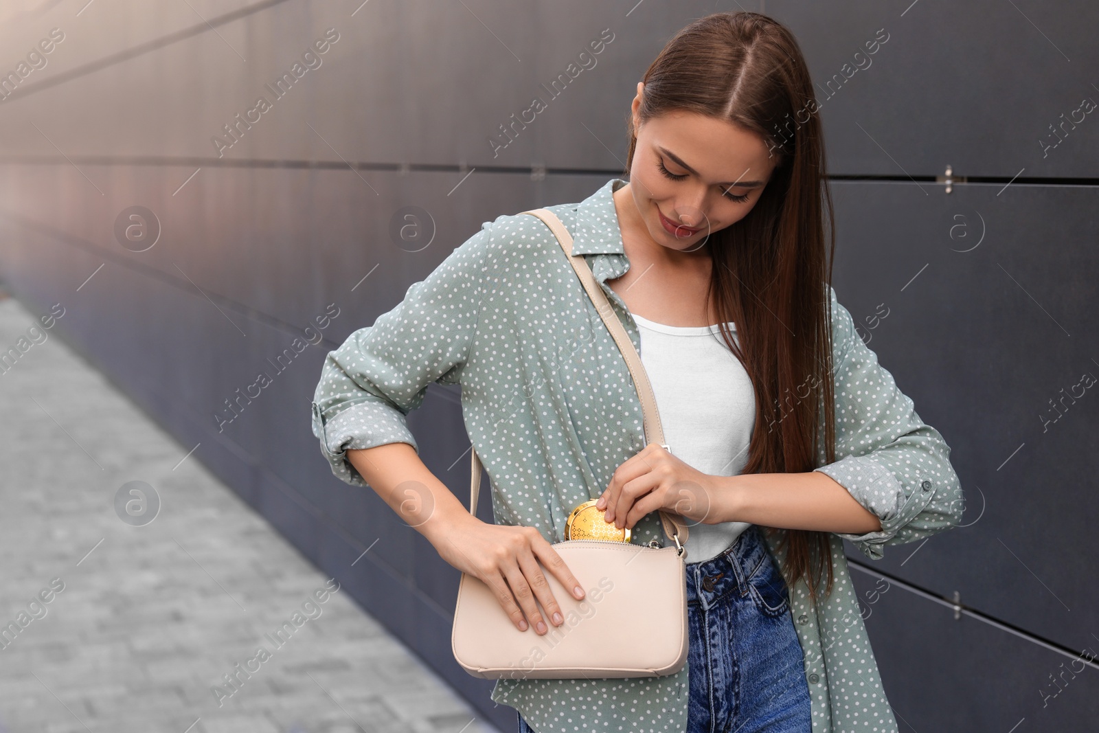 Photo of Woman taking cosmetic pocket mirror from bag outdoors, space for text