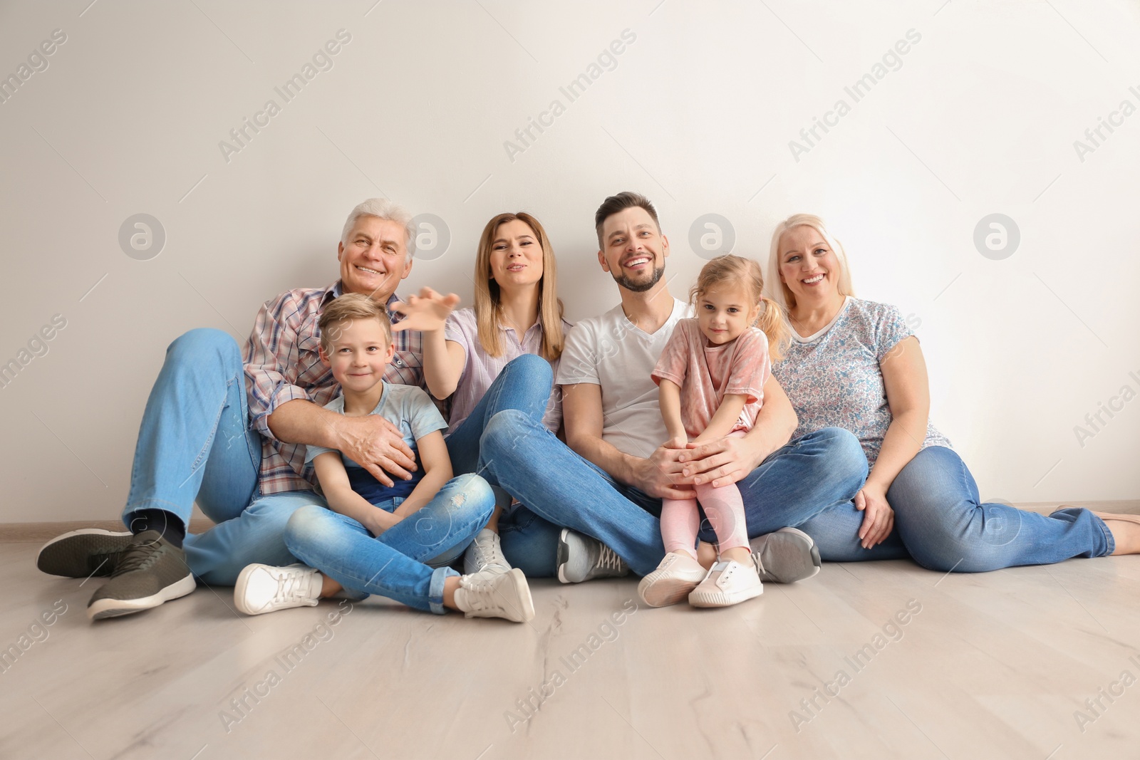 Photo of Happy family with cute kids sitting on floor near light wall