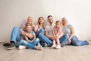 Happy family with cute kids sitting on floor near light wall