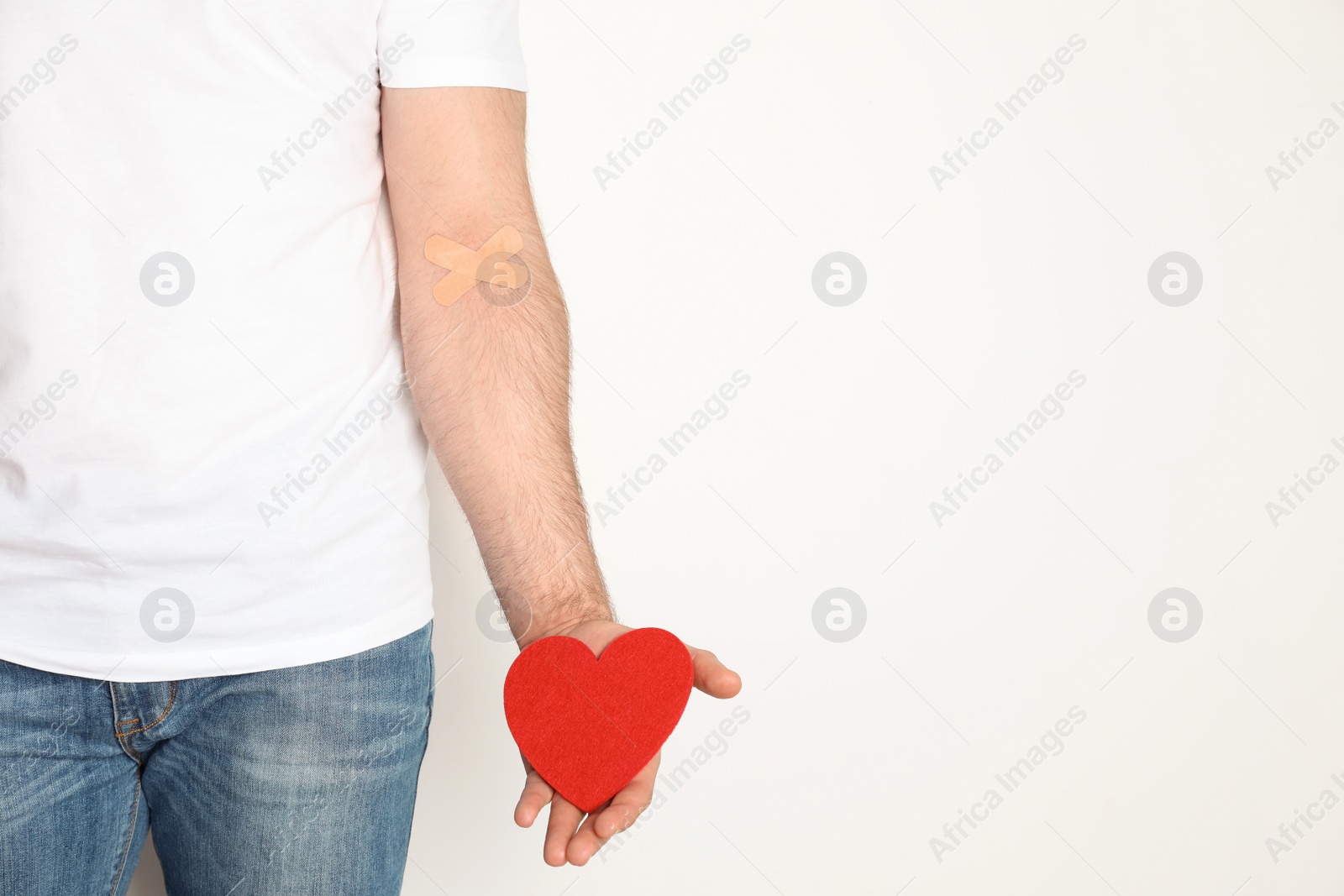 Photo of Man holding heart near hand with adhesive plasters against white background, space for text. Blood donation concept