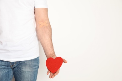 Man holding heart near hand with adhesive plasters against white background, space for text. Blood donation concept