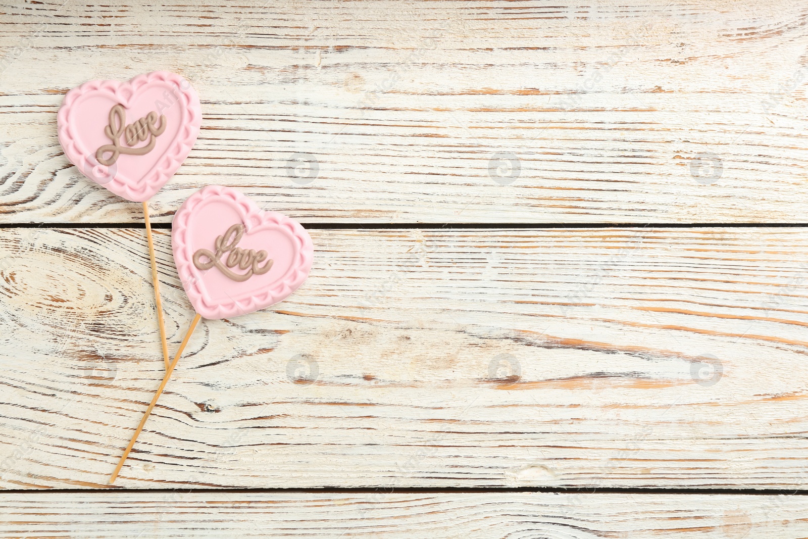 Photo of Chocolate heart shaped lollipops with word Love on white wooden table, flat lay. Space for text