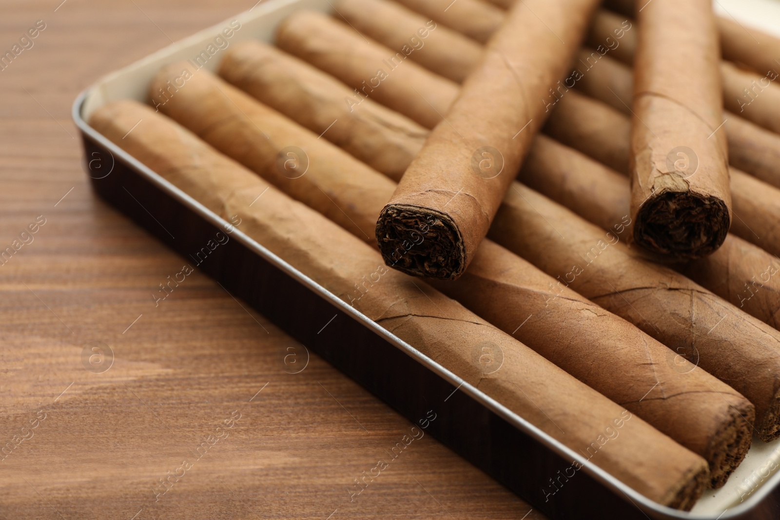 Photo of Many cigars in box on wooden table, closeup