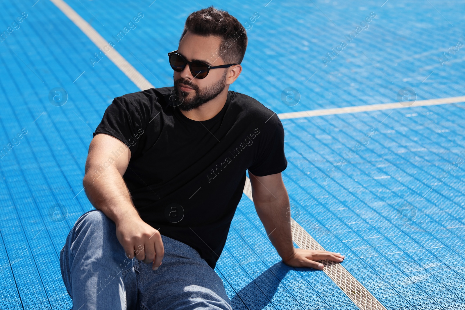 Photo of Handsome man in sunglasses on blue floor covering outdoors, space for text