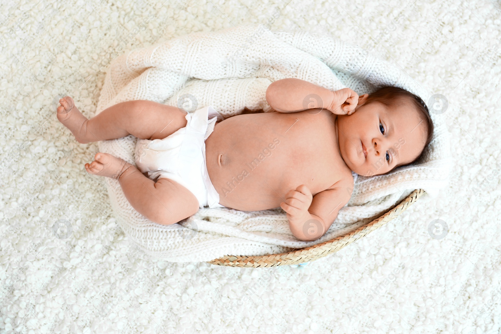 Photo of Cute little baby lying on knitted plaid in cradle, top view