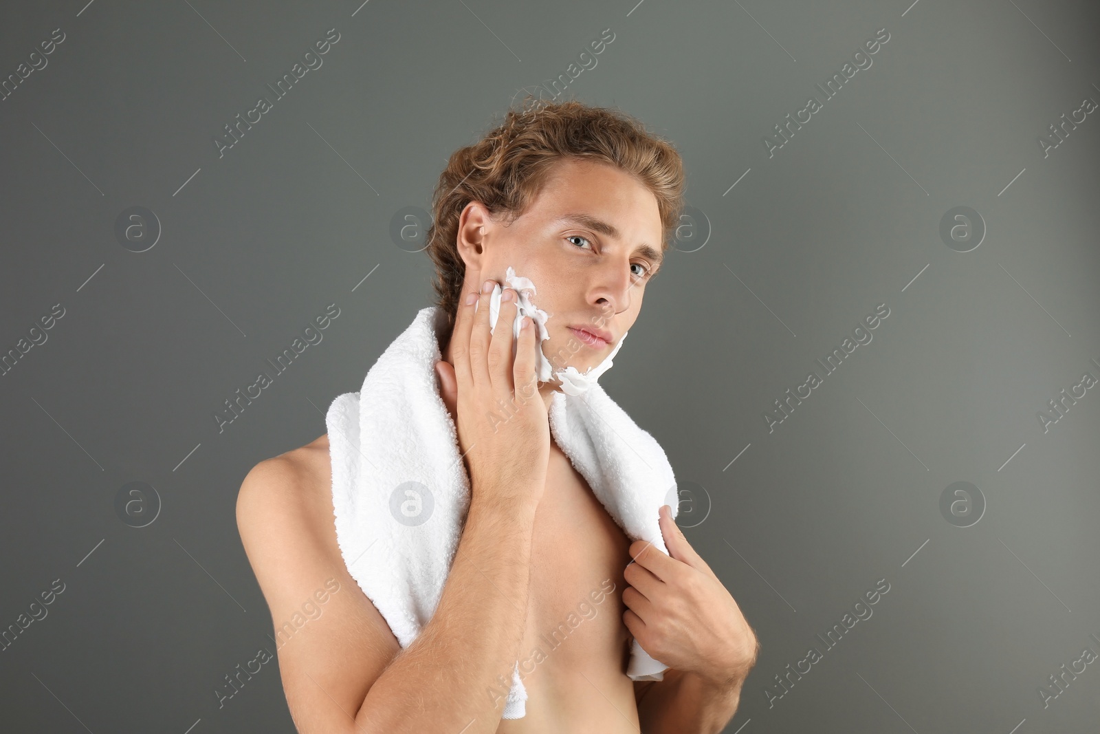 Photo of Young man applying shaving foam on gray background