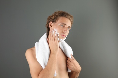 Young man applying shaving foam on gray background