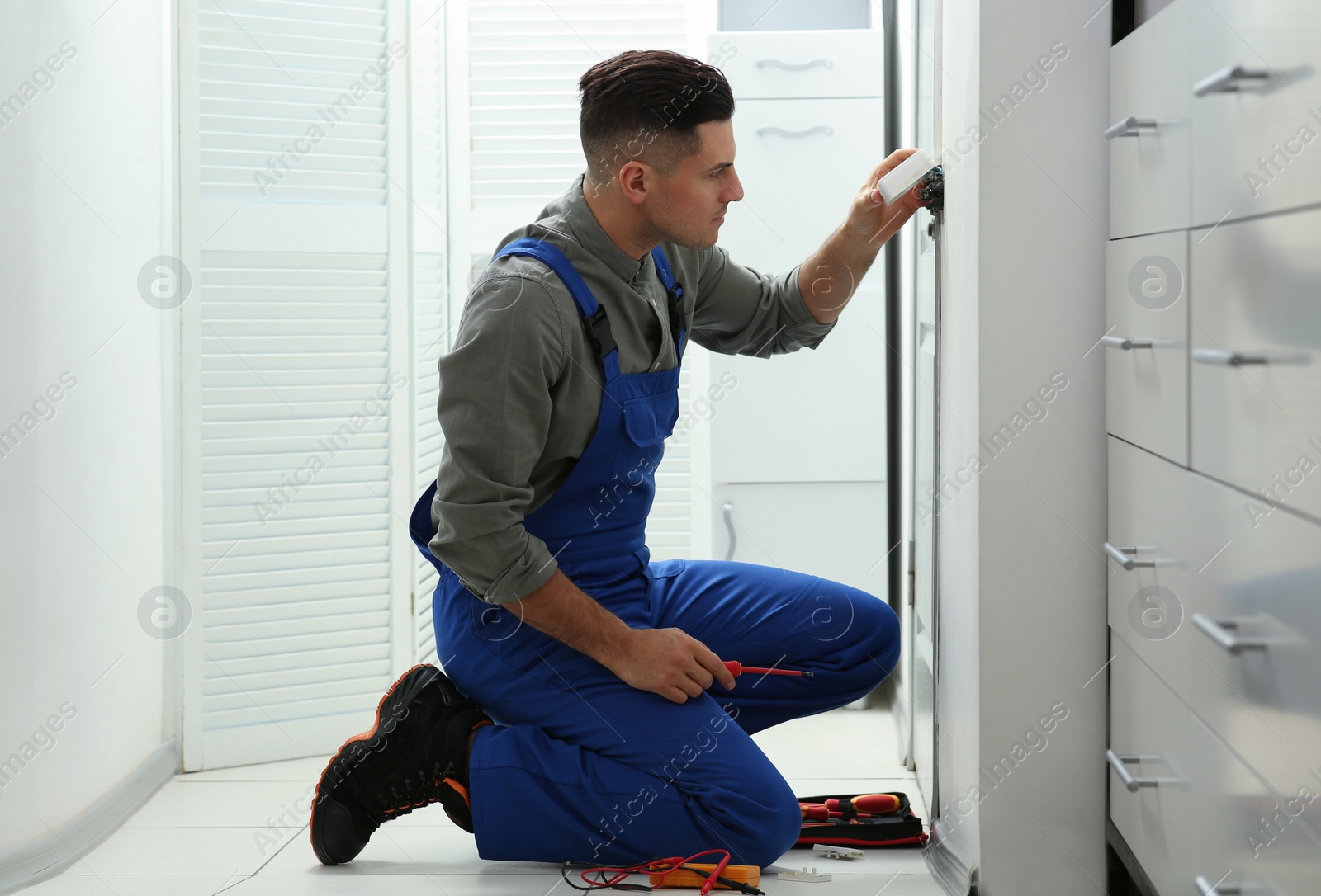 Photo of Professional electrician with screwdriver repairing light switch indoors