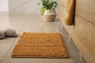 Soft orange bath mat and slippers on floor indoors