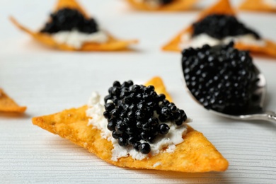 Photo of Chips with black caviar and cream cheese on white wooden background, closeup