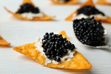 Chips with black caviar and cream cheese on white wooden background, closeup