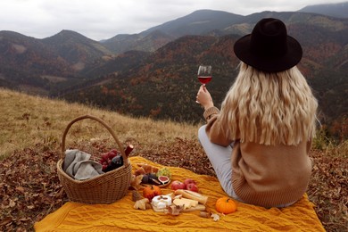 Photo of Young woman with glass of wine having picnic in mountains on autumn day, back view. Space for text