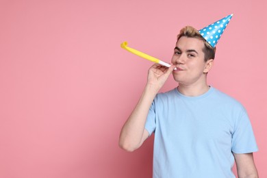 Young man with party hat and blower on pink background, space for text