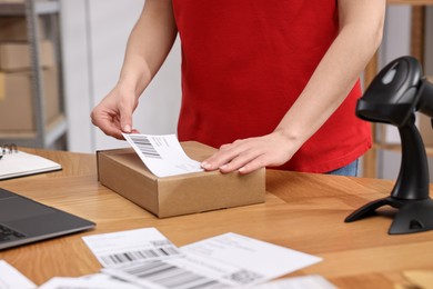 Parcel packing. Post office worker sticking barcode on box at wooden table indoors, closeup