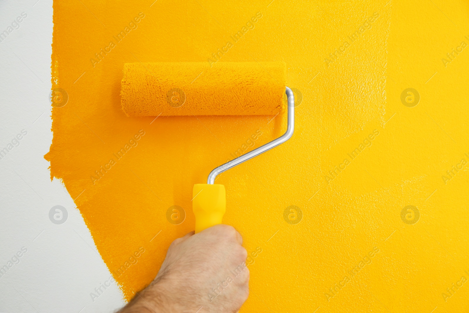 Photo of Man painting white wall with yellow dye, closeup. Interior renovation