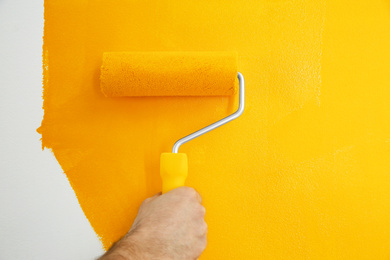 Photo of Man painting white wall with yellow dye, closeup. Interior renovation