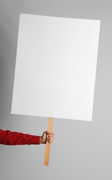 Woman holding blank sign on light grey background, closeup. Space for design