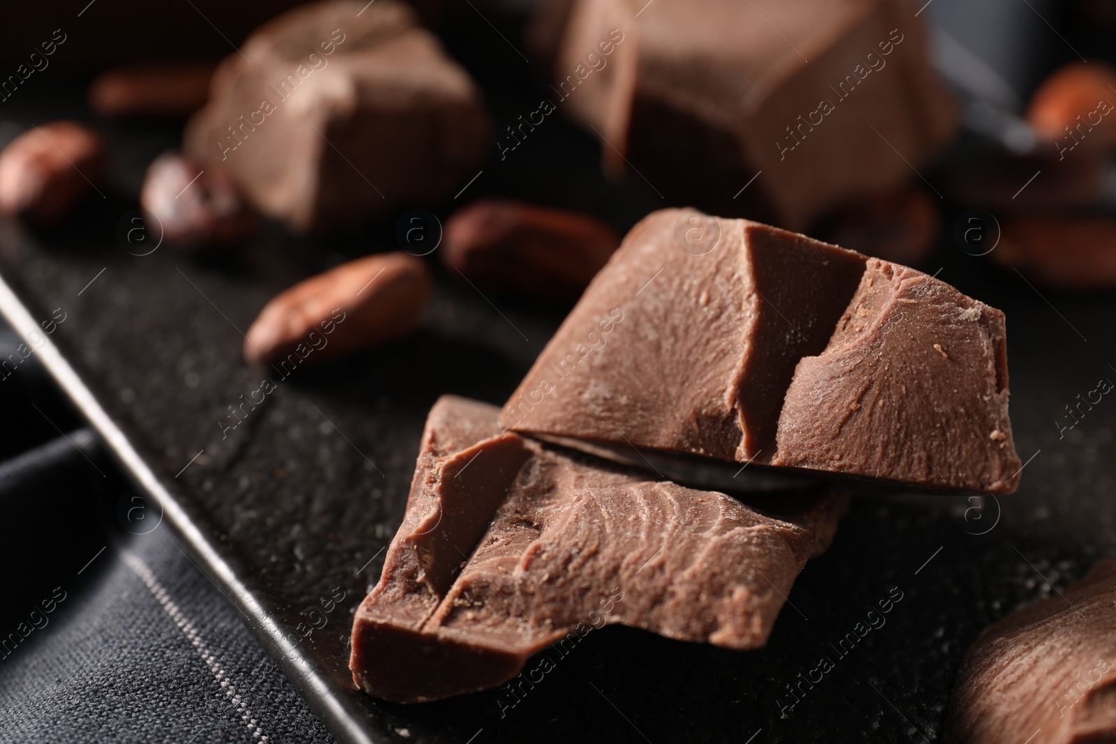 Photo of Pieces of tasty milk chocolate on slate board, closeup