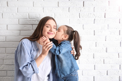 Photo of Young mother and little daughter near white brick wall. Space for text